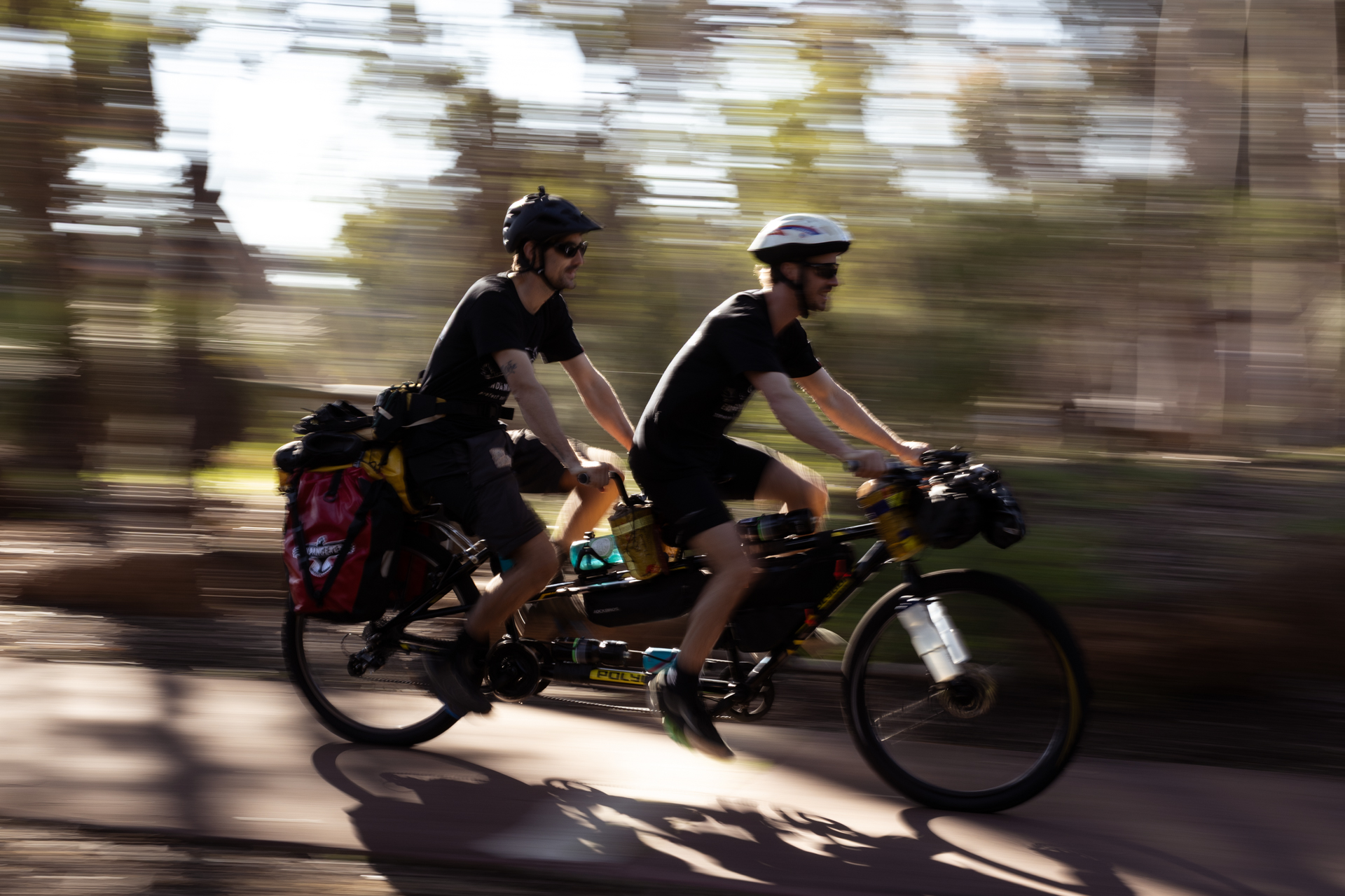 Johno and Kenny riding their tandem bike in a forested area, moving fast.